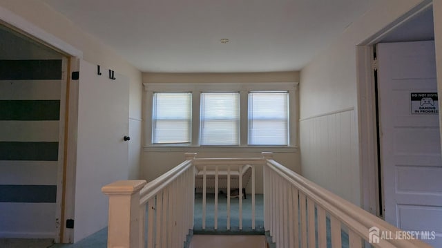 corridor with an upstairs landing, carpet, and a wainscoted wall