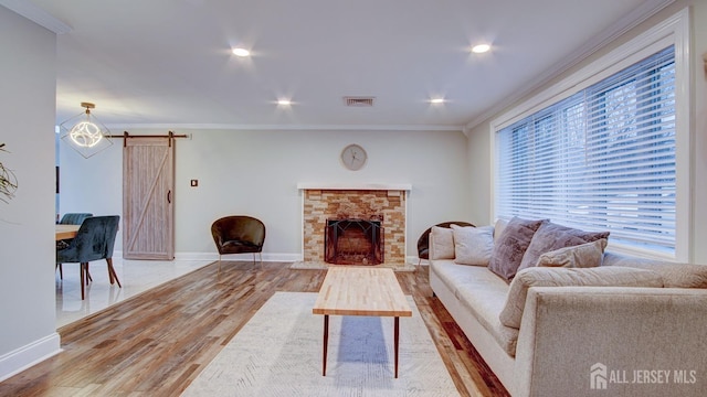 living room featuring a barn door, wood finished floors, visible vents, and ornamental molding