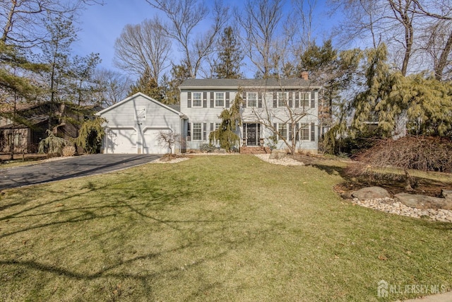 colonial home with an attached garage, driveway, a chimney, and a front yard