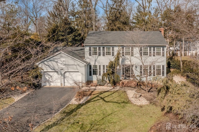 colonial house with aphalt driveway, a front lawn, a chimney, and an attached garage