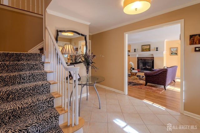 staircase with baseboards, ornamental molding, a fireplace with raised hearth, and tile patterned floors