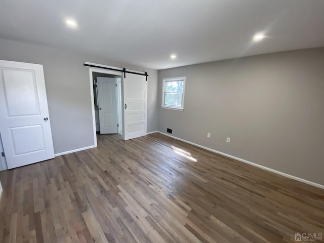 unfurnished bedroom featuring dark hardwood / wood-style flooring and a barn door