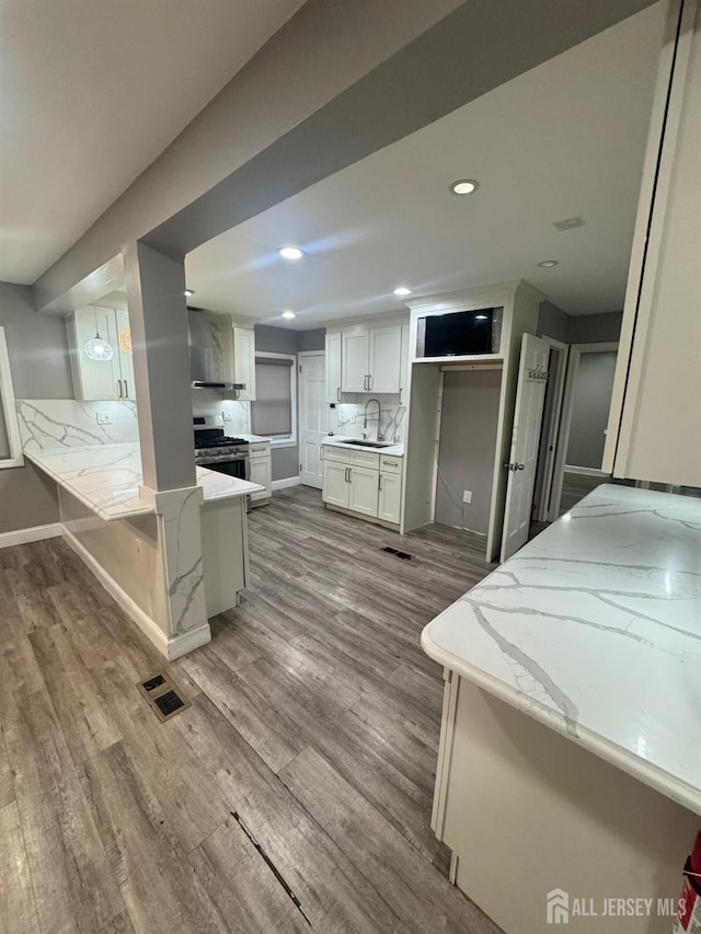 kitchen with stainless steel range with gas cooktop, wood finished floors, white cabinets, a sink, and recessed lighting