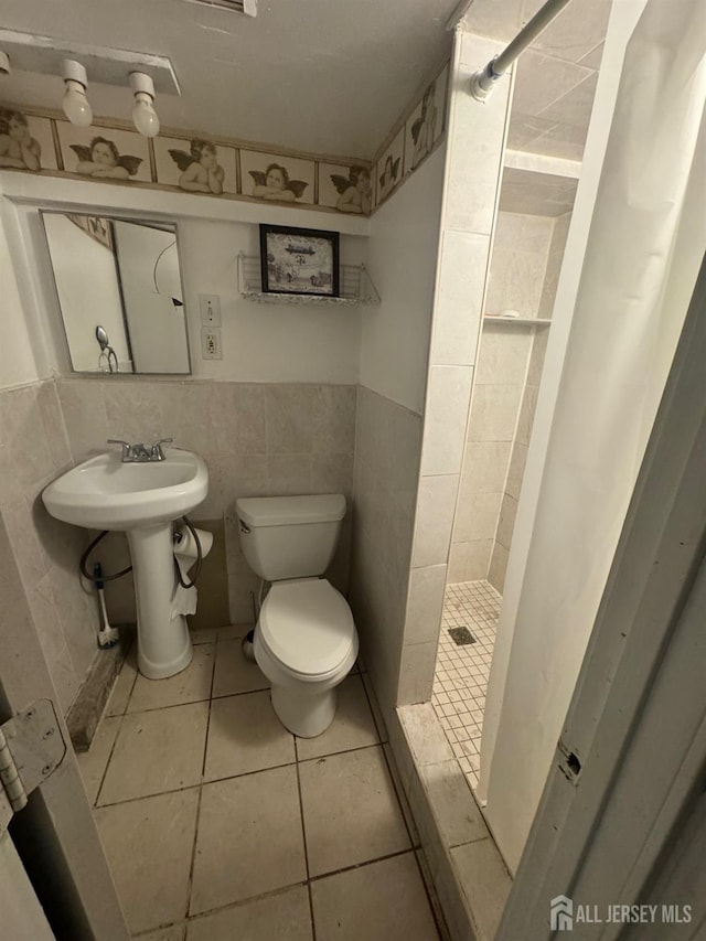 bathroom with toilet, a shower stall, tile walls, tile patterned floors, and a sink