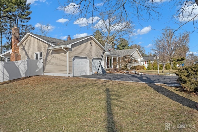 view of property exterior with a chimney, a lawn, an attached garage, fence, and driveway