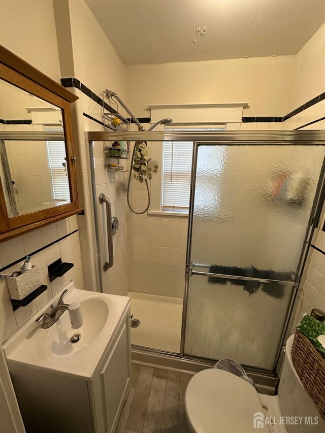 bathroom with hardwood / wood-style flooring, a shower with door, vanity, decorative backsplash, and toilet