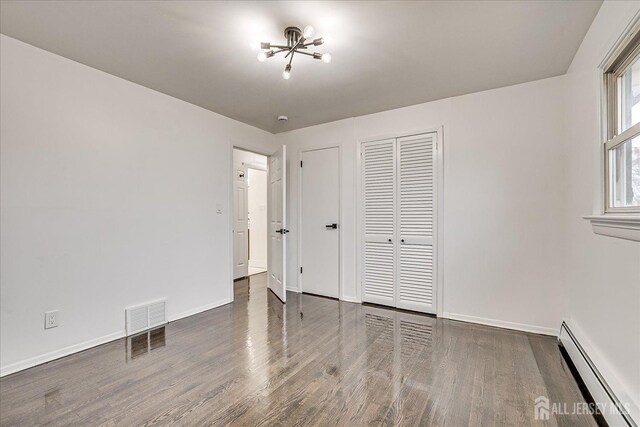 unfurnished bedroom featuring baseboard heating, dark wood-type flooring, and an inviting chandelier