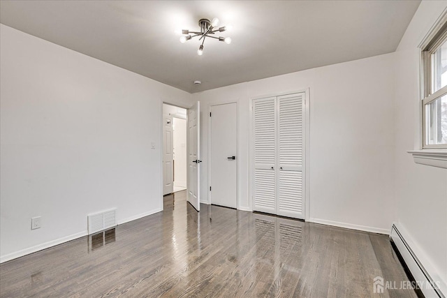 unfurnished bedroom with dark hardwood / wood-style floors, baseboard heating, and a closet