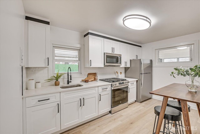 kitchen featuring white cabinets, stainless steel appliances, tasteful backsplash, sink, and light wood-type flooring