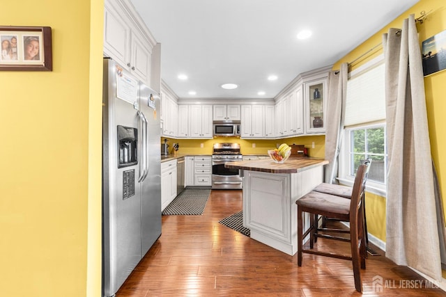 kitchen featuring dark wood finished floors, a kitchen breakfast bar, appliances with stainless steel finishes, and white cabinets