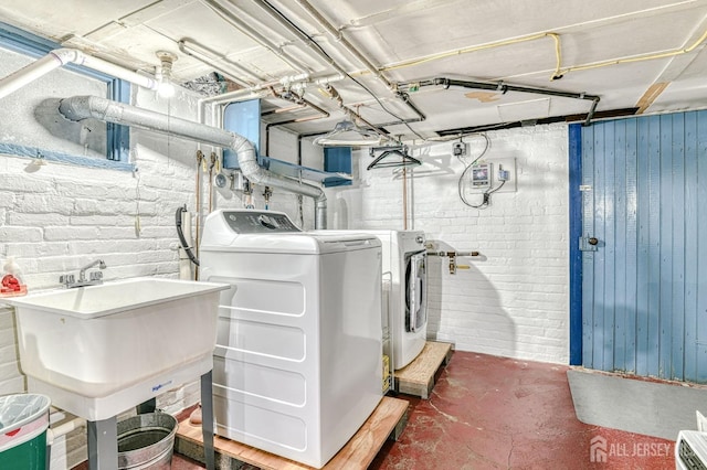 clothes washing area with washer and clothes dryer, laundry area, brick wall, and a sink