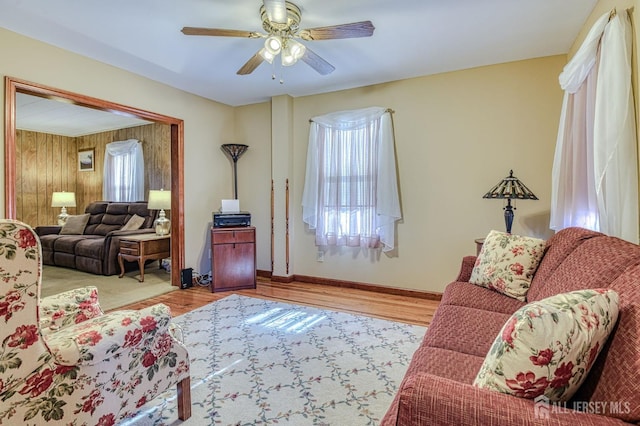 living area with light wood finished floors, wooden walls, baseboards, and ceiling fan