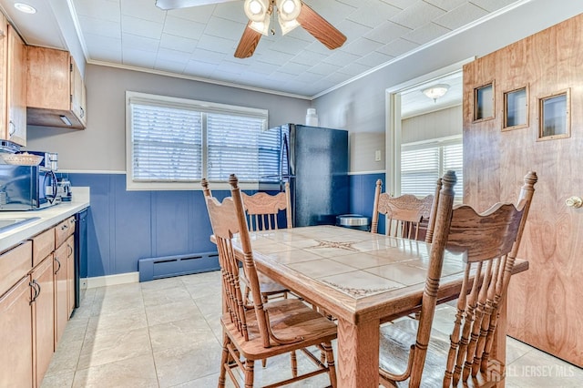 dining area with a baseboard heating unit, ceiling fan, ornamental molding, light tile patterned floors, and wainscoting