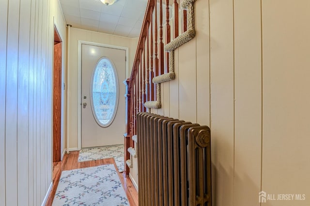 entrance foyer featuring light wood-type flooring, wooden walls, and radiator heating unit