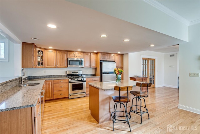 kitchen with a kitchen bar, a sink, light stone counters, appliances with stainless steel finishes, and crown molding