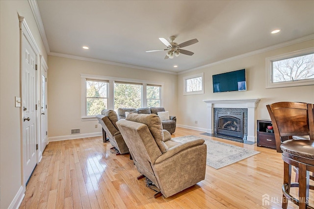 living room with visible vents, a fireplace with flush hearth, ornamental molding, light wood finished floors, and baseboards