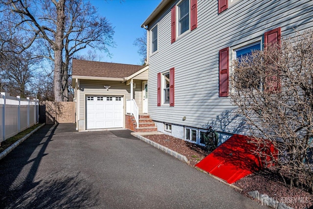 view of side of property with aphalt driveway, an attached garage, and fence