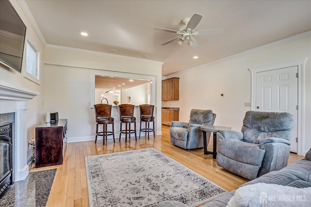 living area featuring a fireplace with flush hearth, light wood-style flooring, a ceiling fan, and ornamental molding