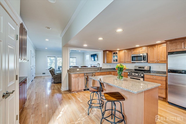 kitchen with light stone countertops, a kitchen island, a breakfast bar, ornamental molding, and appliances with stainless steel finishes