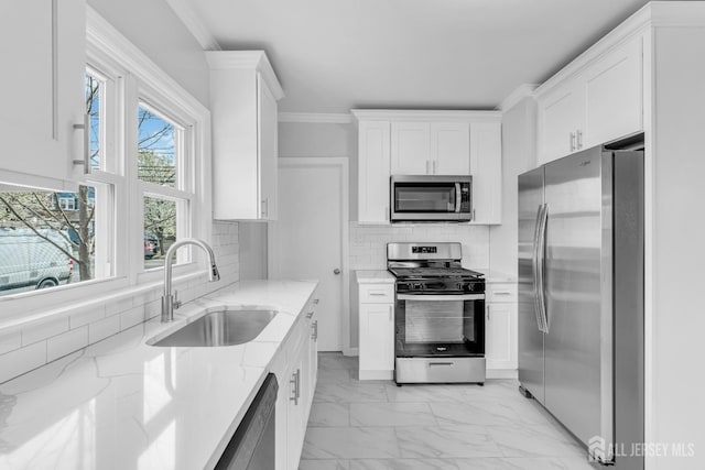 kitchen featuring stainless steel appliances, a sink, light marble finish floors, white cabinets, and ornamental molding