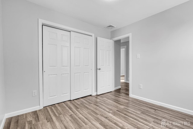 unfurnished bedroom featuring light wood-style flooring, baseboards, and a closet