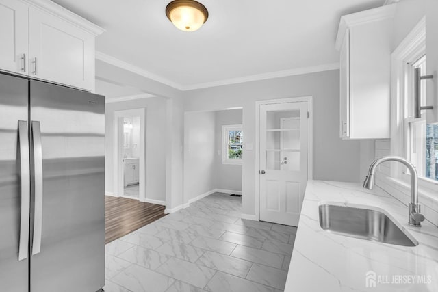kitchen featuring freestanding refrigerator, a sink, marble finish floors, white cabinetry, and light stone counters