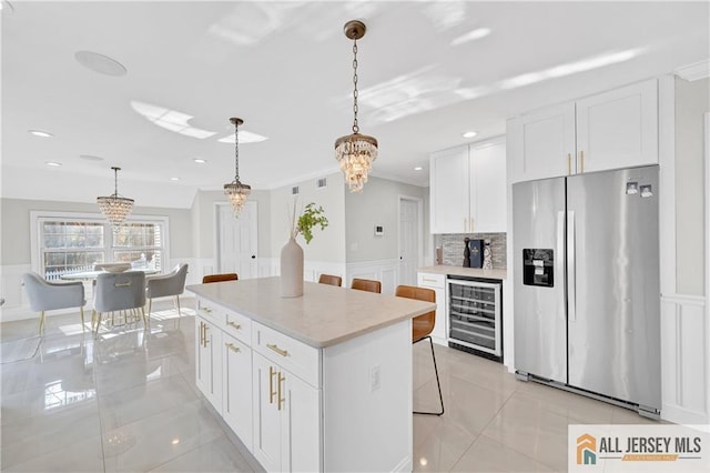 kitchen featuring beverage cooler, decorative light fixtures, white cabinets, stainless steel fridge with ice dispenser, and a center island