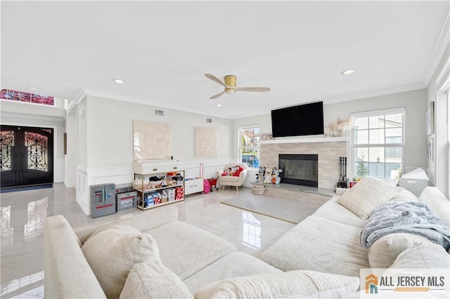 living room featuring a tiled fireplace, ceiling fan, crown molding, and french doors