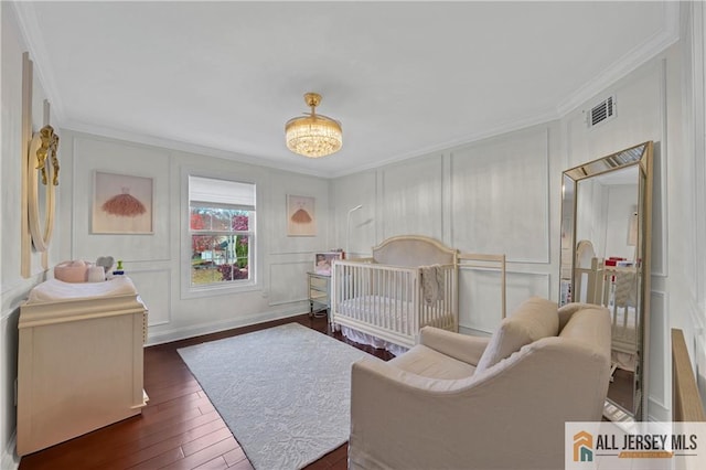 bedroom with a chandelier, crown molding, dark hardwood / wood-style flooring, and a nursery area