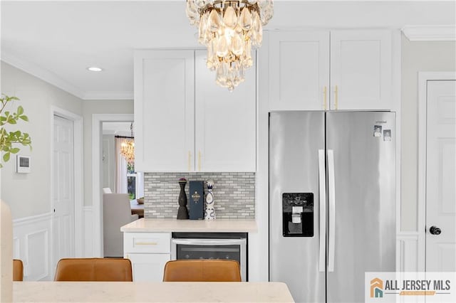 kitchen with white cabinets, crown molding, stainless steel refrigerator with ice dispenser, tasteful backsplash, and a chandelier