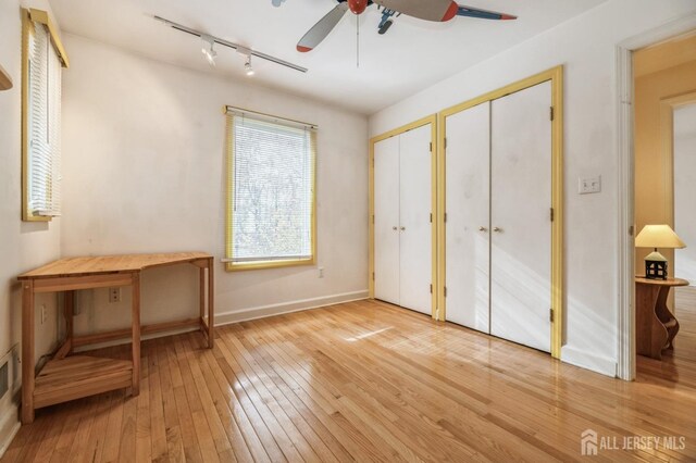 unfurnished bedroom with hardwood / wood-style flooring, ceiling fan, rail lighting, and multiple closets