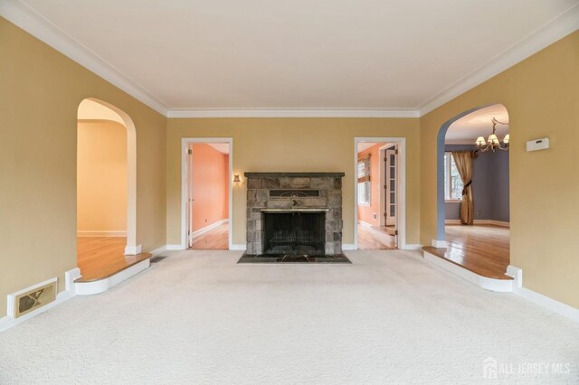 unfurnished living room with hardwood / wood-style floors, a stone fireplace, ornamental molding, and a notable chandelier