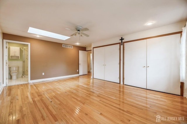 unfurnished bedroom featuring ceiling fan, a barn door, light wood-type flooring, and connected bathroom