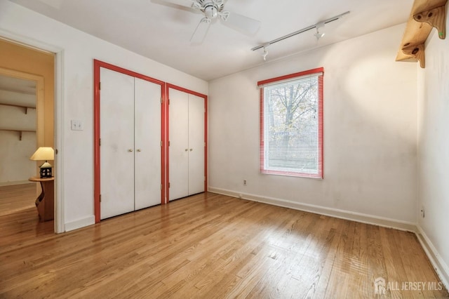 unfurnished bedroom with two closets, ceiling fan, light hardwood / wood-style flooring, and track lighting