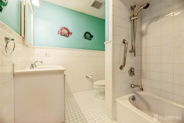 full bathroom featuring vanity, toilet, tile walls, and tiled shower / bath combo