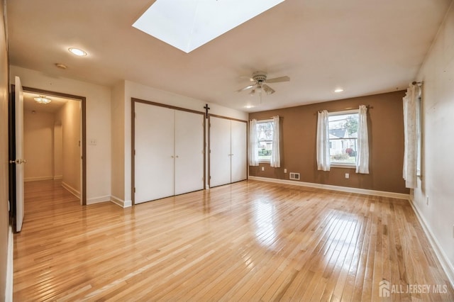 unfurnished bedroom featuring a skylight, ceiling fan, and light hardwood / wood-style flooring