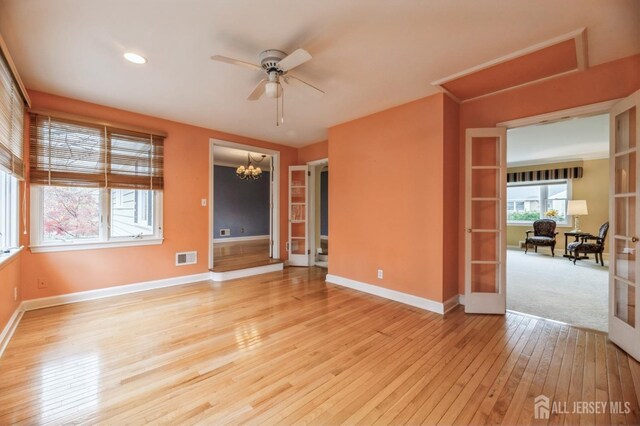 unfurnished room with french doors, ceiling fan with notable chandelier, and light wood-type flooring