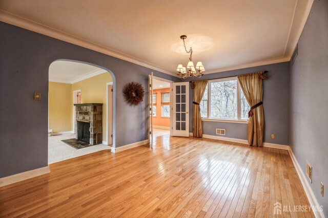 empty room featuring french doors, an inviting chandelier, crown molding, light hardwood / wood-style floors, and a fireplace