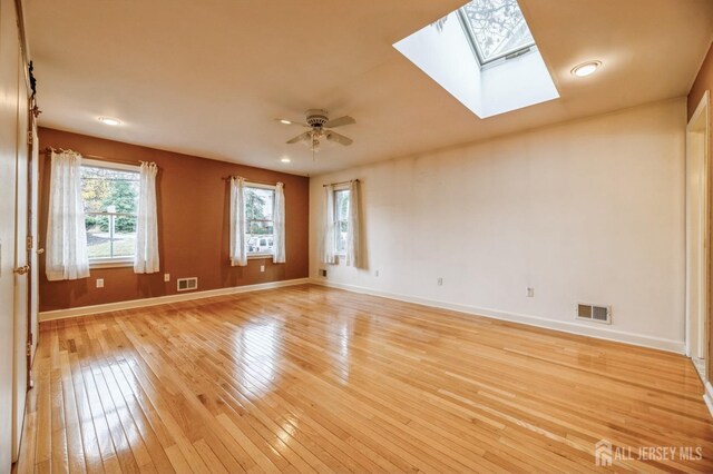 unfurnished room with a skylight, light hardwood / wood-style flooring, and ceiling fan