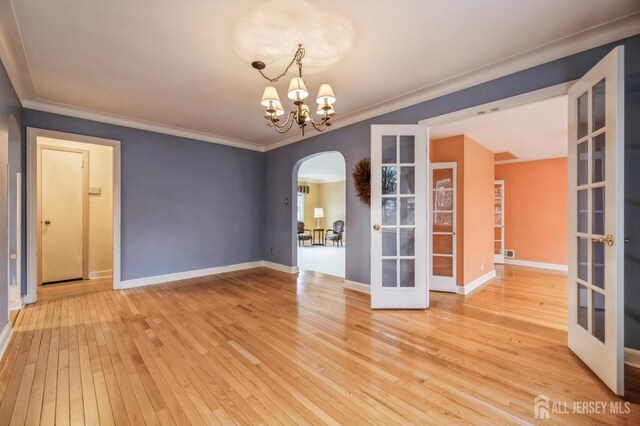 spare room with french doors, an inviting chandelier, ornamental molding, and light hardwood / wood-style flooring