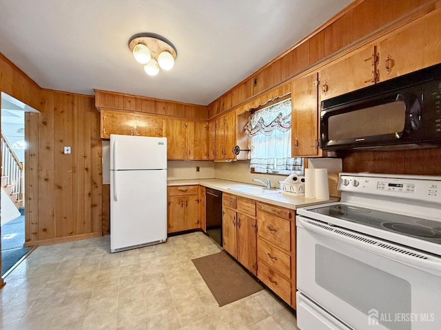 kitchen with light countertops, brown cabinetry, wood walls, a sink, and black appliances