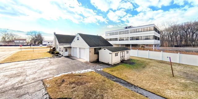 view of front of house featuring an outdoor structure, fence, driveway, and a front lawn