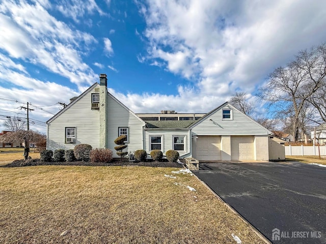 view of front of property with a front lawn, fence, aphalt driveway, a chimney, and a garage