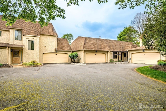 view of front facade with an attached garage, roof with shingles, and stucco siding