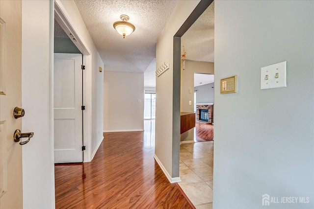 hallway featuring baseboards, light wood-type flooring, and a textured ceiling