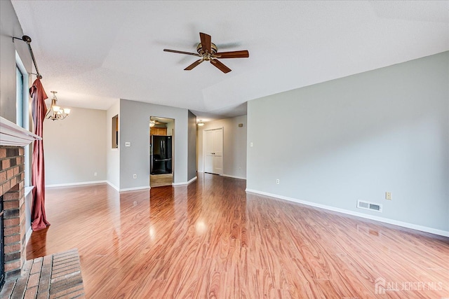 unfurnished living room featuring light wood-style floors, a fireplace, ceiling fan with notable chandelier, baseboards, and visible vents