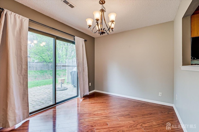 unfurnished room featuring baseboards, an inviting chandelier, wood finished floors, and visible vents