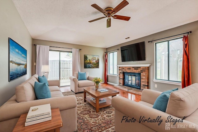 living area with plenty of natural light, a brick fireplace, ceiling fan, and wood finished floors