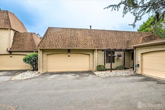 view of front of property featuring stucco siding, a garage, a shingled roof, and aphalt driveway