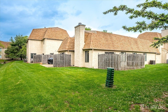 rear view of property with stucco siding, fence, a yard, and a chimney